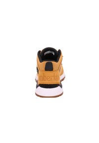 Czarno-żółty sneakers z teksturowaną cholewką, wyściełanym kołnierzem i wyraźną metką na pięcie z wytłoczonym logo. Biała i brązowa podeszwa.