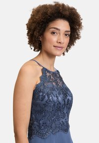 Robe sans manches bleu avec une superposition en dentelle ornée de broderies florales, d'accents en perles et d'un corsage ajusté. Jupe en satin lisse.