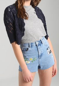 Granatowy dzianinowy bolerko z koronkowym wzorem; szary t-shirt; jasnoniebieskie, przetarte szorty jeansowe z kwiatową haftowaną ozdobą i łatą.