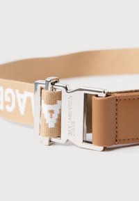 Cinto de tecido bege com texto branco e fivela de metal prateada gravada "Karl Lagerfeld Jeans" fixada a um laço de couro castanho.