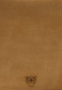 Smeđa suđena površina s malim mjedenim prstenom s dva detaljna ptice koje se suočavaju jedna s drugom blizu donjeg centra.