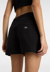 Shorts in denim nero con vita alta, due tasche posteriori e un'etichetta con il logo Vans cucita, dallo stile pulito e minimalista.