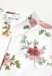 Blouse à col blanc avec imprimé floral rose et orange et feuilles vertes, avec une étiquette de la marque MNG partiellement visible.