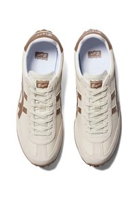 Beżowe sneakersy z brązowymi akcentami, z teksturowaną górą, płaskimi sznurowadłami i logo na języku. Klasyczny design z gładkim wykończeniem.