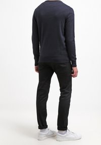 Granatowy sweter dziewiarski z okrągłym dekoltem, w połączeniu z dopasowanymi czarnymi dżinsami i białymi sneakersami, charakteryzujący się gładką teksturą i prostym fasonem.