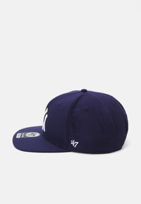 Gorra de béisbol de color azul marino con visera plana, que presenta un logotipo y texto bordados en blanco, y un tejido texturizado. Etiqueta presente en el lado.