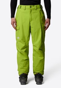 Klart gröna vattentäta skidbyxor med cargofickor, justerbart midjeband och avslappnad passform, i kombination med svarta skidstövlar.