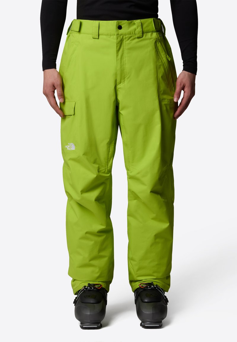 Klart gröna vattentäta skidbyxor med cargofickor, justerbart midjeband och avslappnad passform, i kombination med svarta skidstövlar.