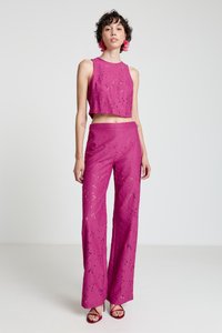 Fuchsia two-piece set featuring a sleeveless crop top and wide-leg pants with a textured pattern and cut-out details. Heels complete the look.