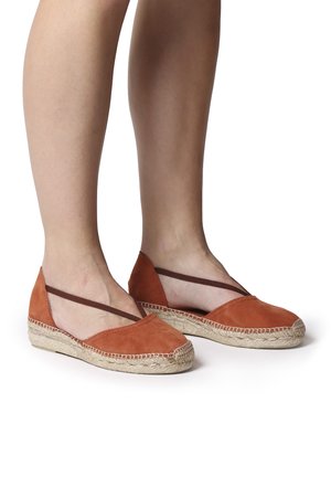 Suede espadrilles in rust color with brown elastic straps. Woven jute soles feature a textured edge. Flat, rounded toe design.