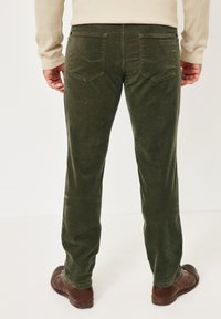 Olivgrüne Cordhosen mit sichtbaren Nähten, gerade geschnittenem Bein und zwei Gesäßtaschen. Mattierte Textur, getragen mit braunen Schuhen.