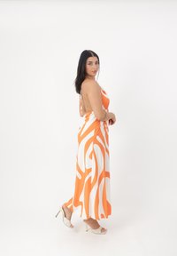 Maxi kjole i orange og hvid med et bølget mønster, halterneck, åben rygdesign og glat tekstur. Sammen med lette hæl-sandaler.