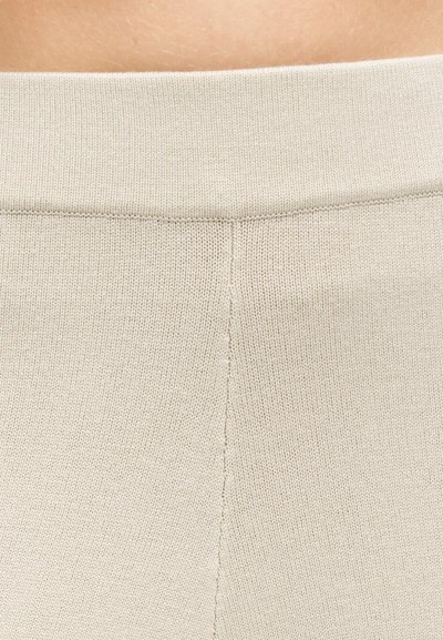 Κοντινή λήψη ζώνης από πλεκτό μπεζ ύφασμα με κεντρική κάθετη ραφή σε ανοιχτόχρωμο δέρμα.