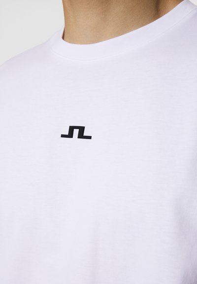 Hvit bomulls t-skjorte med en liten svart geometrisk logo på brystet, rund hals og myk tekstur.
