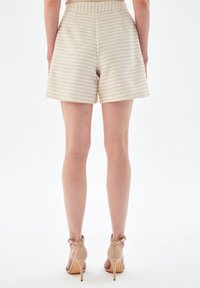 Béžové texturované šortky s horizontálními pruhy, s vysokým pasem a volným střihem. V kombinaci s neutrálními sandály na vysokém podpatku.