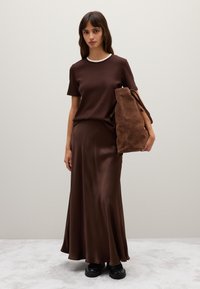 Maglietta corta marrone con colletto bianco, abbinata a una gonna lunga di raso marrone. Borsa a spalla in suede marrone e scarpe con plateau nere.