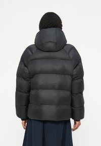 Sort puffjakke med en tætsiddende hætte, prydet med et quiltet design og elastiske manchetter. Glat ydre med en let skinnende overflade.
