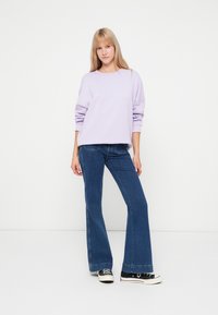 Μωβ φούτερ με ελεύθερη εφαρμογή, στρογγυλή λαιμόκοψη και χαμηλωμένα μανίκια, συνδυασμένο με μπλε φαρδιά τζιν και μαύρα καμβά παπούτσια.