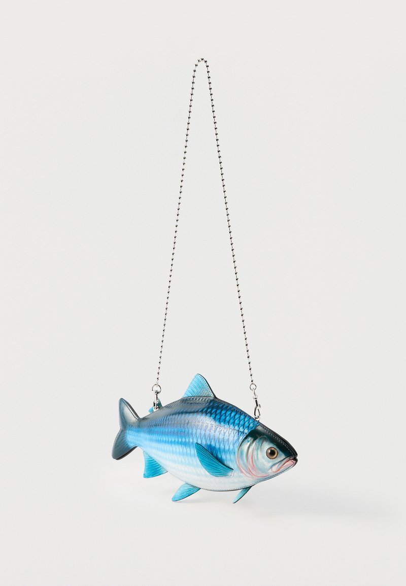 Sac à main en forme de poisson bleu et argenté avec des écailles et des nageoires détaillées, suspendu à une fine bandoulière en chaîne argentée sur un fond blanc.