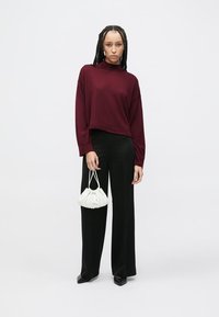Bluza burgundy cu mâneci lungi, pantaloni largi negri și o geantă plisată albă. Ținuta are un croi lejer și texturi de țesătură netede.