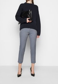 Maglione lavorato a maglia blu navy, pantaloni cropped a fantasia in blu e bianco, tiene una pochette in pelle nera ed indossa scarpe con tacco nere.