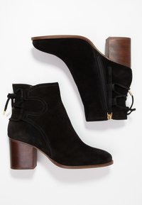 Botas de tobillo de ante negro con punta redondeada, tacones de bloque de madera y cremallera lateral. Presentan un detalle anudado y costuras en contraste.