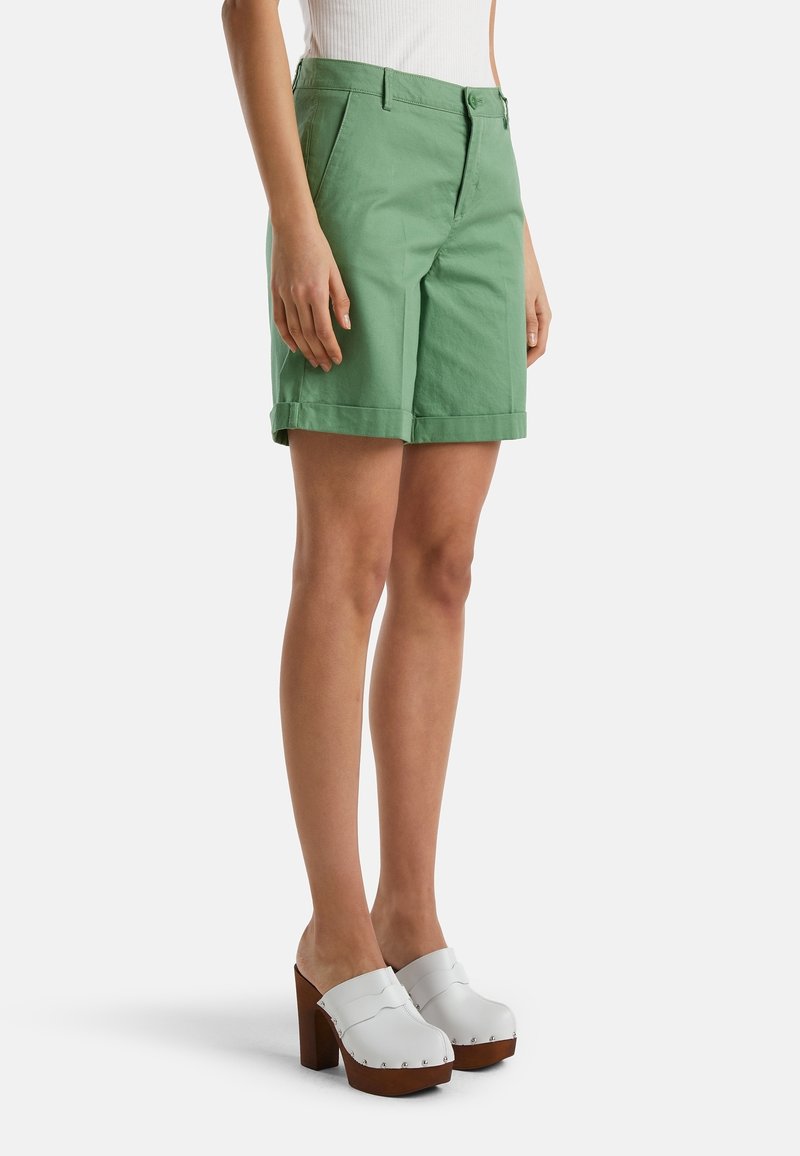 Zelené bavlněné šortky s rovnými předními částmi, poutky na opasek a ohrnutými lemy. V kombinaci s bílými dřeváky s platformou.