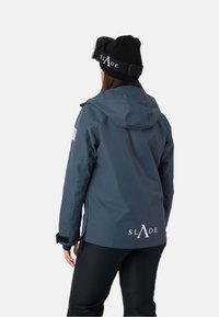 Mörkgrå vattentät jacka med huva, som har en vit logotyp på ryggen och svarta detaljer vid muddarna och fickorna.