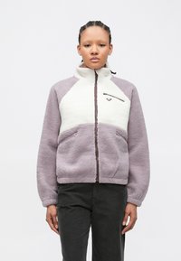 Fleece jacket with a high collar; purple and cream color blocks; front zip pocket; textured fabric; relaxed fit with side pockets.