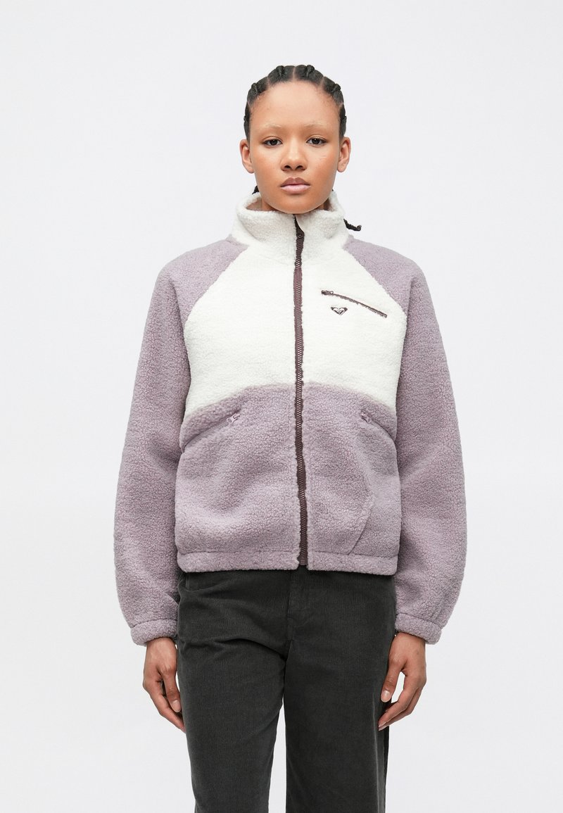 Fleece jacket with a high collar; purple and cream color blocks; front zip pocket; textured fabric; relaxed fit with side pockets.