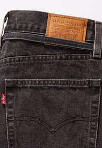 Mørkegrå denimjeans med strukturert overflate, med et lærmerke på livlinjen og en rød logoklipp på baklommen.