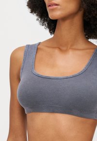 Grå ribbad bralette med fyrkantig halsringning och breda remmar. Mjuk textur med diskret stretch och en sömlös design för komfort.