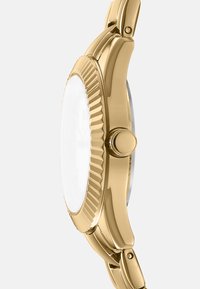 Orologio oro con una lunetta scanalata, superficie liscia, vetro trasparente e quadrante rotondo che mostra dettagli minimi. Accenti argentati sul cinturino.