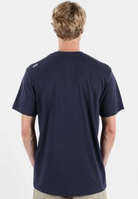 T-shirt en coton bleu marine à manches courtes, col rond, avec un petit logo sur l'épaule, vu de dos.