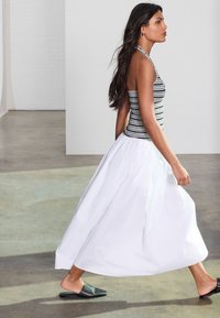 Sort og hvid stribet halterneck-top med en let hvid maxi-nederdel i let stof, kombineret med sorte slip-on mule-sko.