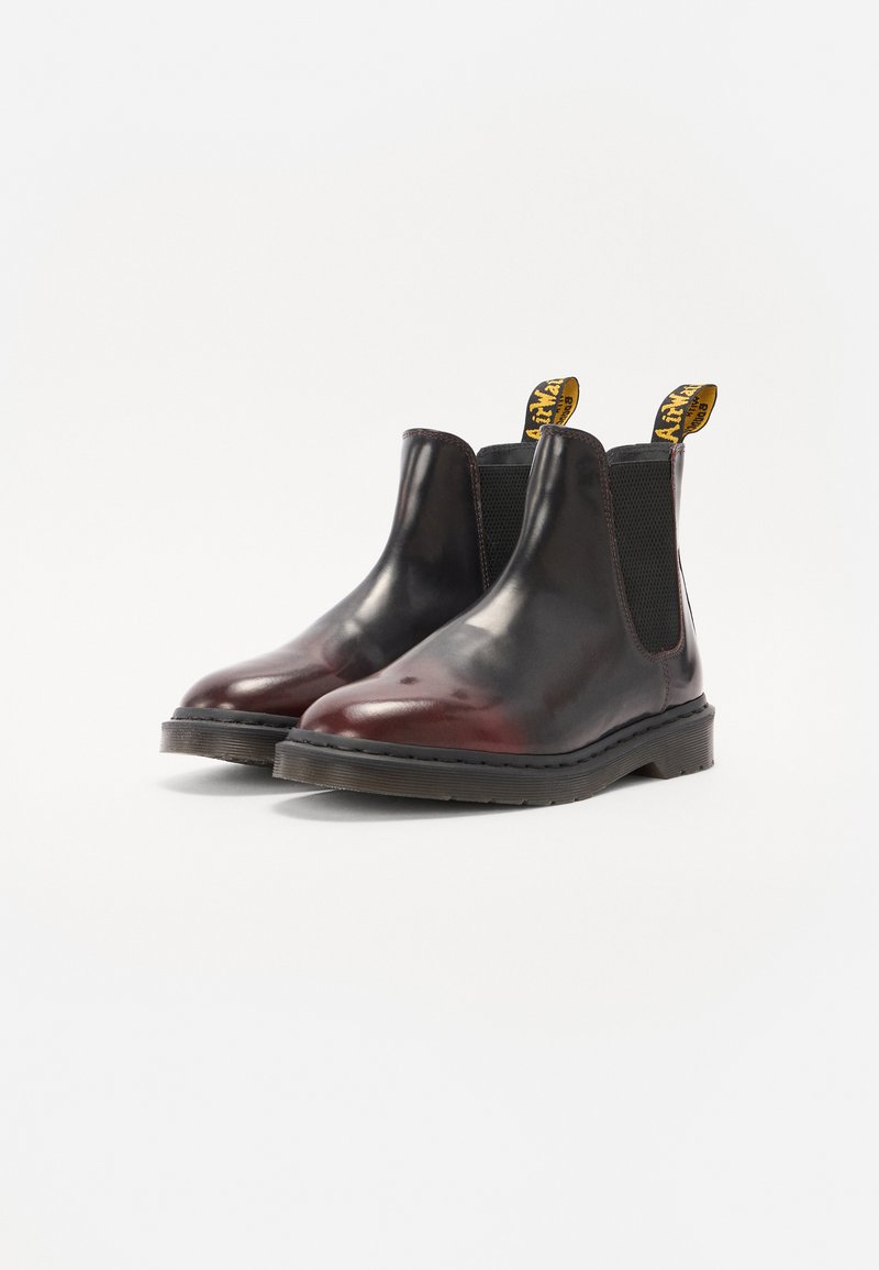 Botas Chelsea de cuero negro y burdeos con paneles laterales elásticos, puntera redonda y suelas de goma resistentes; presenta tiradores amarillos con marca.