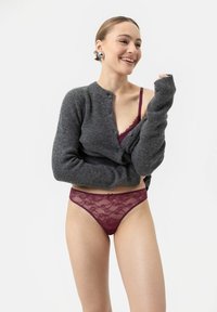 Grå stickad cardigan med knapplåsning, lager på lager över en bourgognylons spets-bh och matchande genomskinlig spetsstring, på en modell mot en vit bakgrund.
