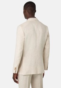 Chaqueta de traje de lino beige con solapas muescas, ventilación trasera sencilla y distintivos acentos de botones dorados en las mangas. Tela suave y texturizada.