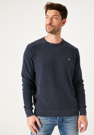 Navyblauwe gestructureerde gebreide trui met een ronde hals en geribbelde manchetten en onderrand. Voorzien van een klein logo op de linkerkant van de borst.