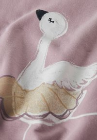 Ilustración de un cisne sobre una tela rosa suave, que presenta un cisne blanco con acentos negros y un detalle de falda dorada con volantes.