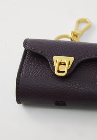 Pochette in pelle viola con chiusura a toggle dorata, superficie testurizzata e cuciture a contrasto lungo i bordi. Design compatto e chiuso.