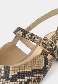 Close-up of beige and brown snakeskin-patterned shoe with gold buckle and ankle strap on a light background.