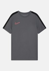 Camiseta atlética gris de mangas cortas, con acentos negros en los hombros y un logo de Nike rosa en el lado izquierdo del pecho. Textura de tela suave.