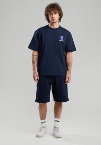 Navy blue cotton t-shirt and matching shorts. T-shirt features a graphic with "NEW YORK" printed in light blue. White sneakers and striped socks.