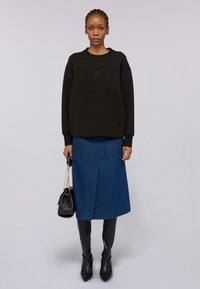 Svart oversized sweatshirt med logodetalj, matchad med en blå denim midi-kjol med fickor. Svarta knähöga spetsiga stövlar och handväska.