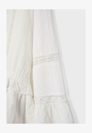 Tissu blanc texturé avec détails en dentelle et sections froncées, probablement une partie d'une manche ou d'une robe.