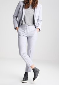 Light gray tailored suit with slim-fit pants, paired with a gray t-shirt and black high-top sneakers. Smooth fabric and simple design.