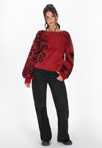 Maglione rosso con stampa leopardo nera e righe; tessuto testurizzato e morbido. Abbinato a jeans neri a gamba larga e scarpe nere.