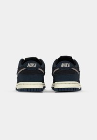 Tenisky Nike s tmavě modrým syntetickým svrškem s texturovanými detaily, krémovou mezipodešví a gumovou podešví. Logo je viditelné na patě.