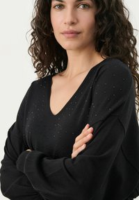 Maglione nero a scollo a V realizzato in tessuto leggero, con maniche lunghe e dettagli decorativi in perle sul petto per texture e interesse visivo.